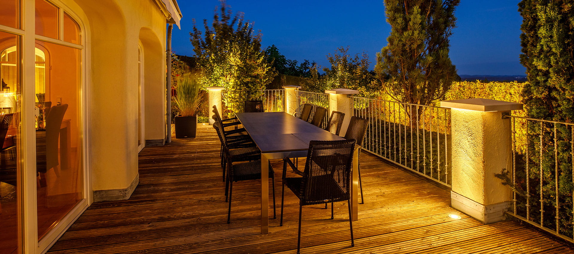 Mediterrane Gartengestaltung mit warmweißer LED-Gartenbeleuchtung: Naturstein, Olivenbaum und Wasser im Abendlicht