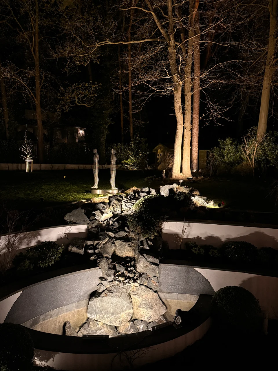 Wasserfall und beleuchtete Baumkronen im Berliner Garten