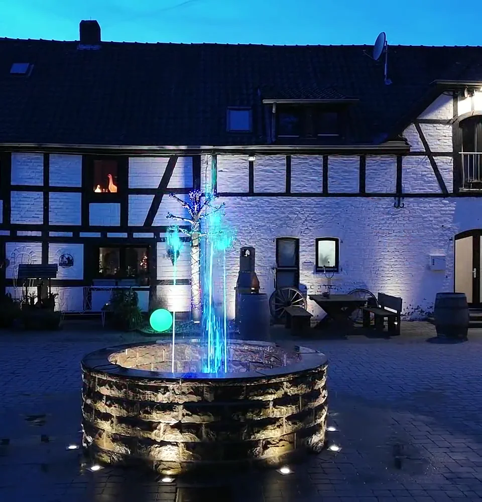 Beleuchteter Brunnen vor dem Fachwerkhaus auf Gut Asselborn in der blauen Stunde.
