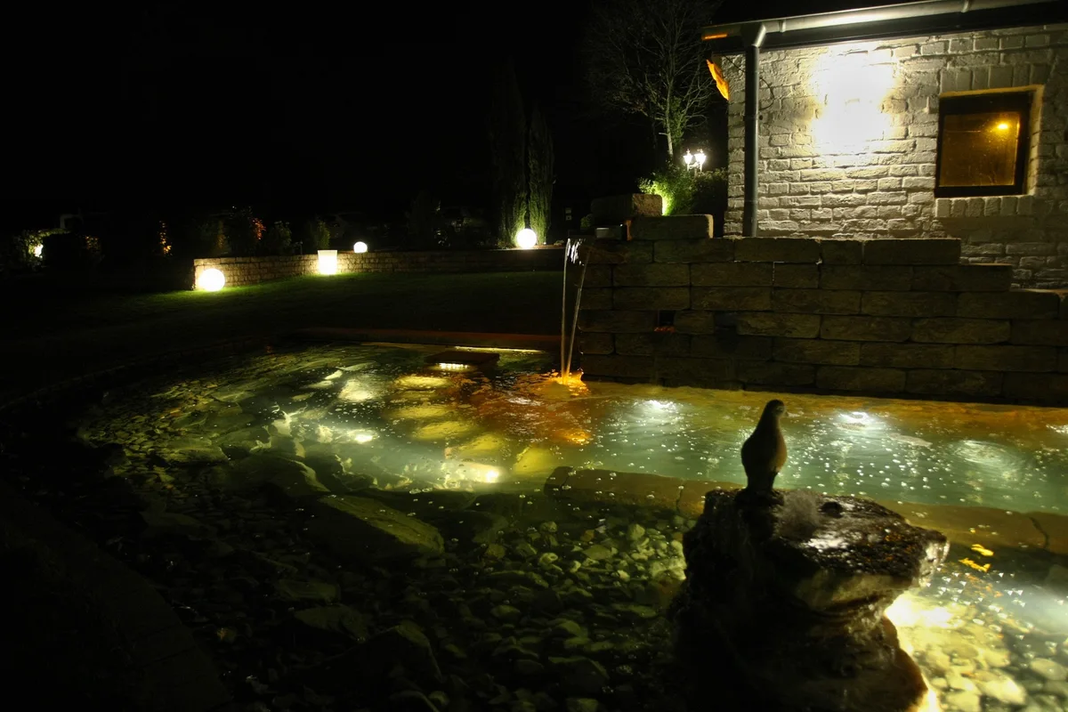 Warmes Licht spiegelt sich im Wasser vor einer Natursteinmauer auf Gut Asselborn.